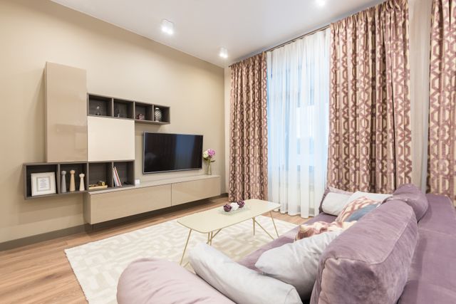 Modern small living room color ideas showing warm beige walls paired with a mauve sofa and patterned curtains