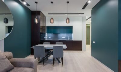 A modern small living room dining room combo featuring teal accent walls, a grey dining set under three glass pendant lights, and a sleek kitchen in the background.