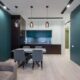 A modern small living room dining room combo featuring teal accent walls, a grey dining set under three glass pendant lights, and a sleek kitchen in the background.
