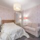 Pink damask bedroom with tufted headboard, blush sofa, and mirrored vanity