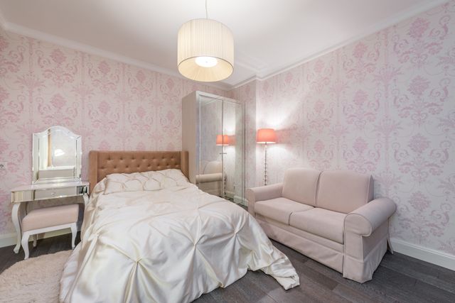 Pink damask bedroom with tufted headboard, blush sofa, and mirrored vanity