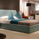 Teal upholstered bed frame with matching throw pillows and walnut nightstand in a modern bedroom showroom