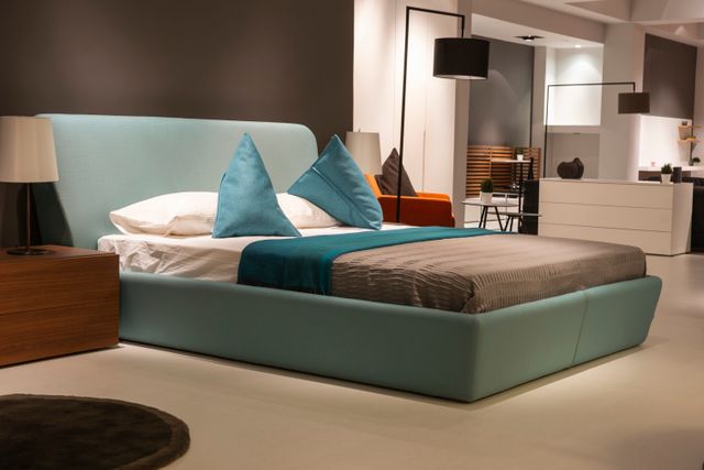 Teal upholstered bed frame with matching throw pillows and walnut nightstand in a modern bedroom showroom